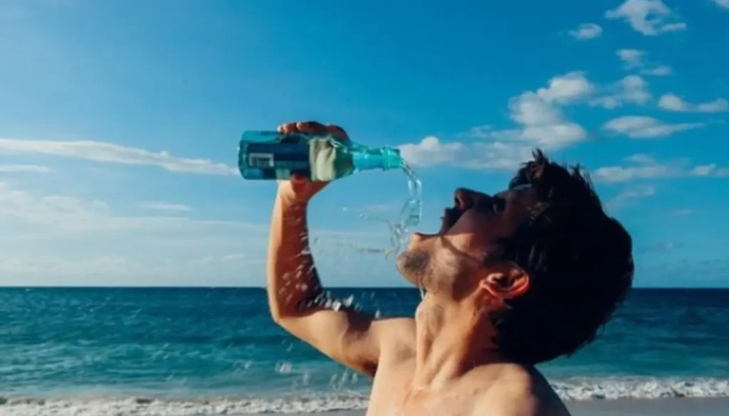 Persona bebiendo agua Agua de mar con la playa de fondo